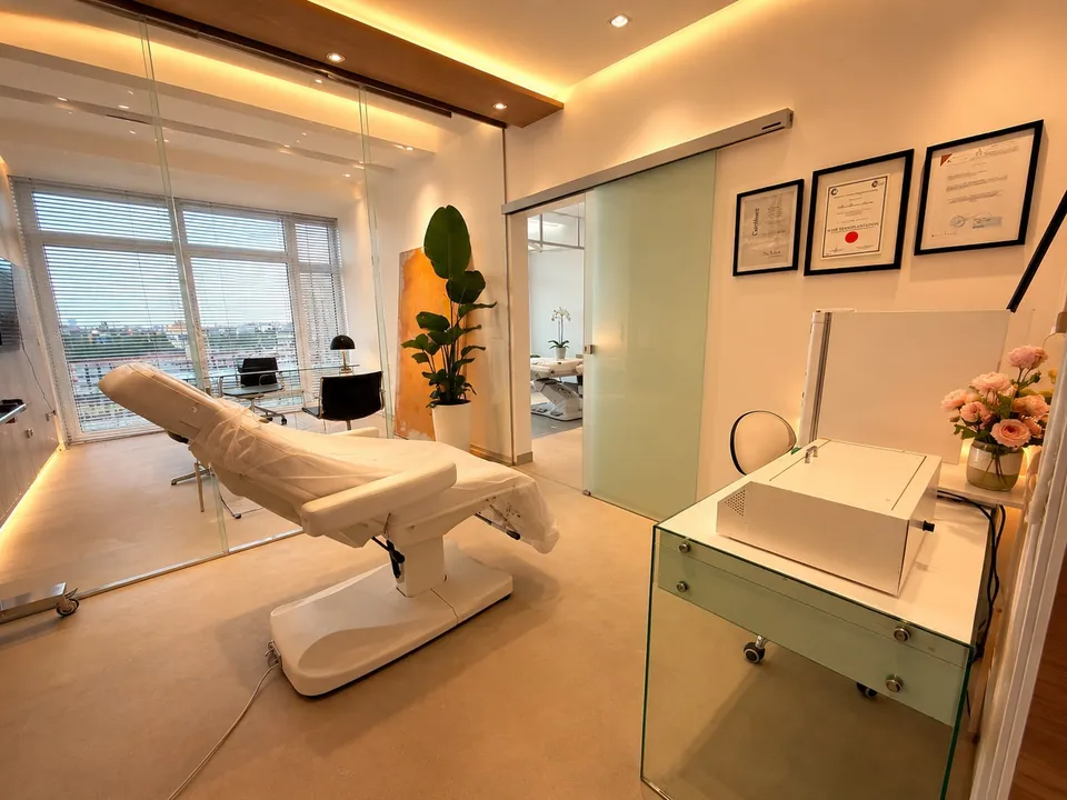 Behandlungsraum der AS Clinic mit Behandlungsliege und gerahmten Zertifikaten an der Wand